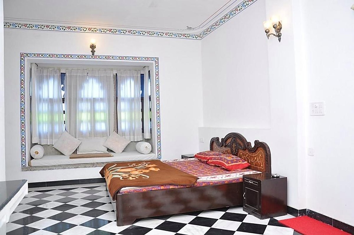 A guest room with a carved wooden bed and the haveli's black-and-white checkered stone floor