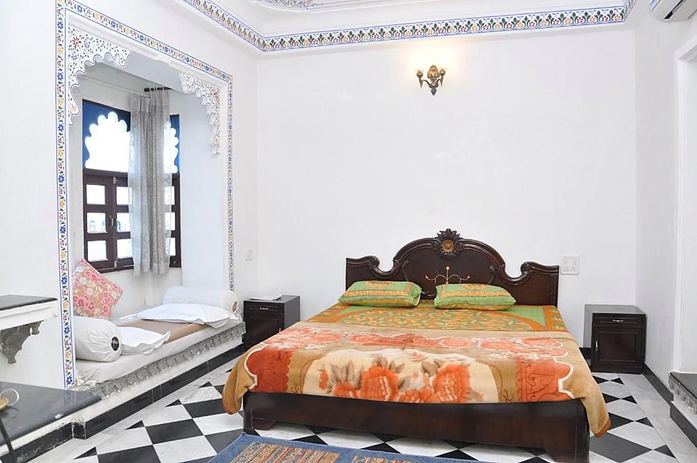 Deluxe Room with Jharokha &mdash; a double bed with a carved headboard, arched window alcove and black-and-white checkered floor