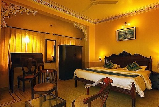 An ochre-walled guest room lit by lamplight with a writing desk and chairs beside the bed