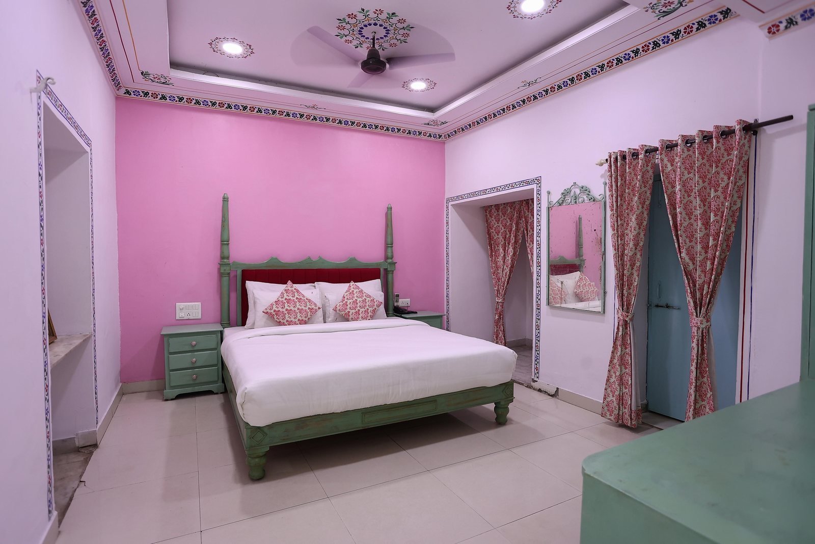 A high-ceilinged guest room with pale rose walls, painted cornice and a wooden bed
