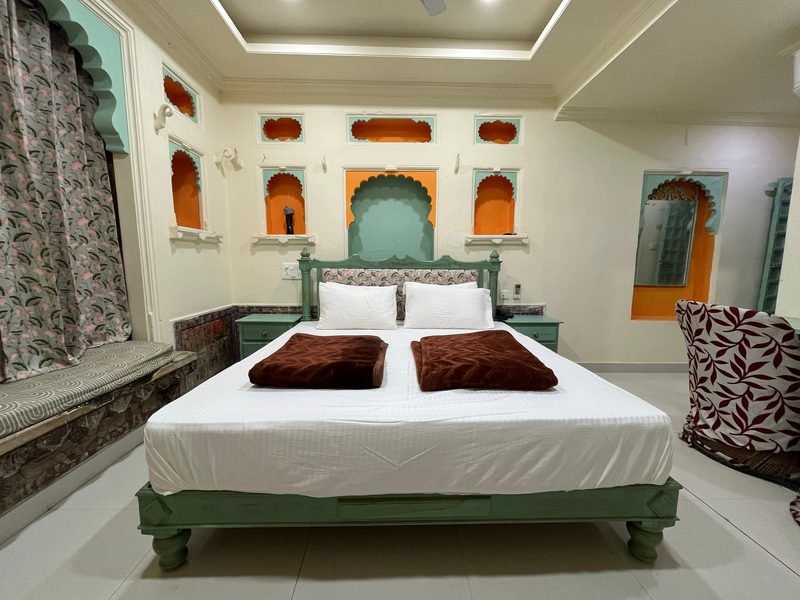 A heritage room with carved wall niches, a cusped arch above the bed and a panelled ceiling