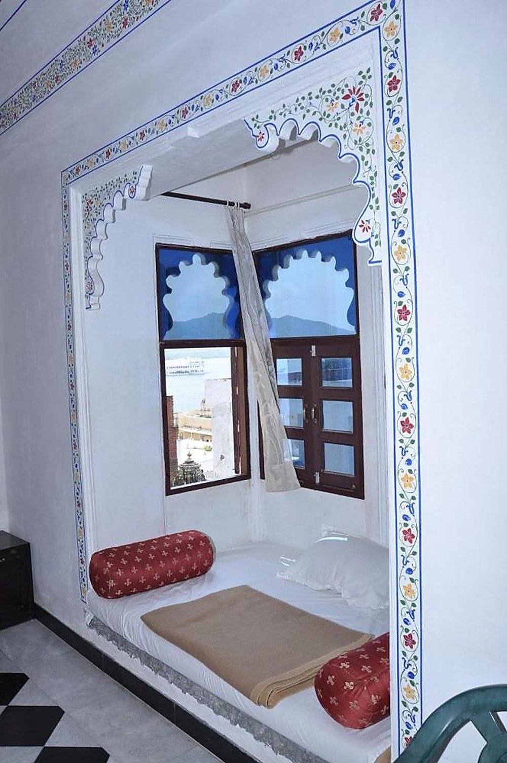 A cushioned window seat set into the thickness of the haveli wall beneath a cusped arch