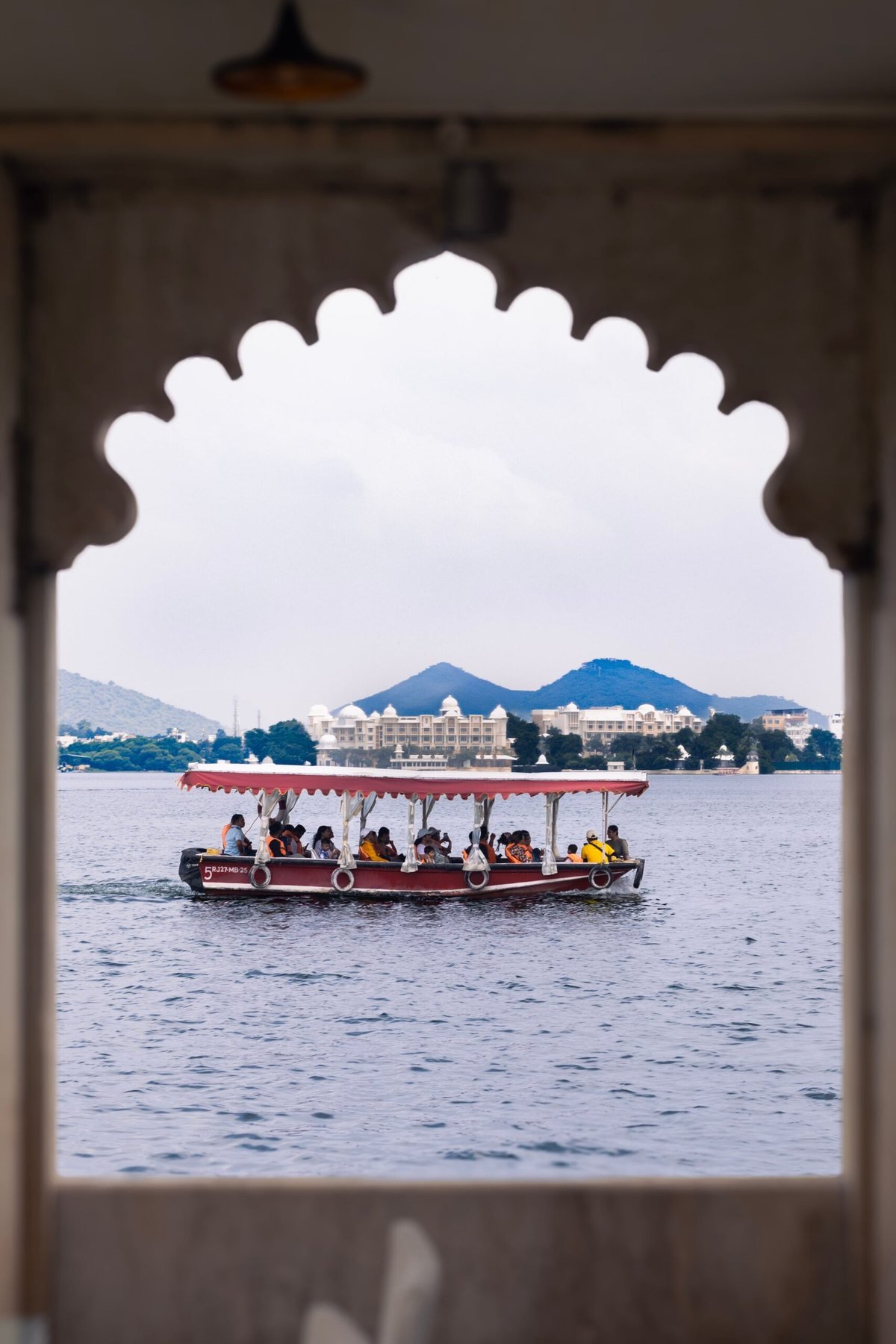 A boat crossing Lake Pichola seen through a cusped arch, with the Lake Palace on the water behind it